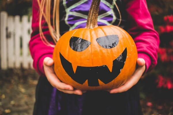 A girl dressed as a witch holding a pumpkin