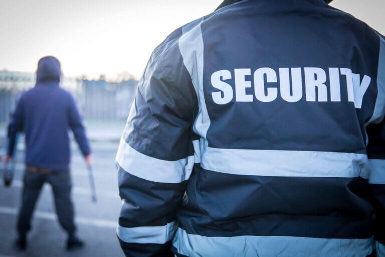 Rear view of RGM Security guard confronting hooded criminal holding metal bar