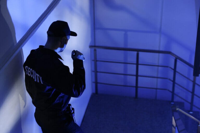 Mobile security guard with torch carrying out night patrols on stairs of local authority site