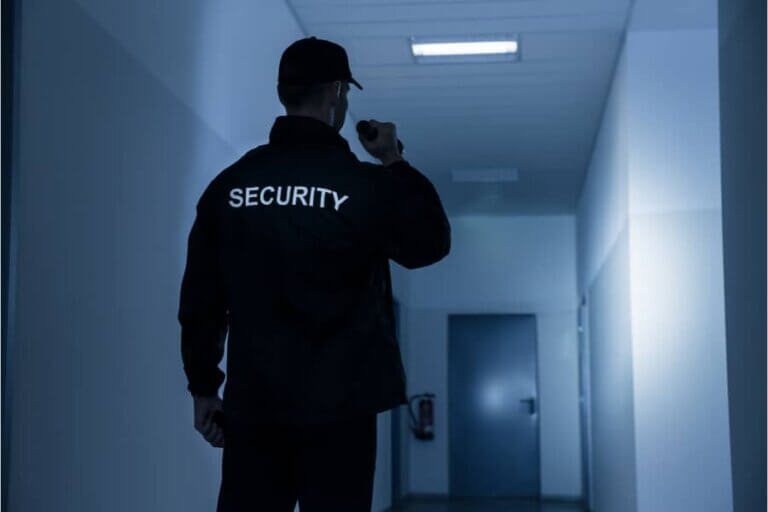 Manned Security guard on night patrols in corridor of building with torch