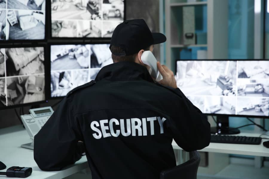 Security Guard on the telephone in front of 5 CCTV Security Monitors