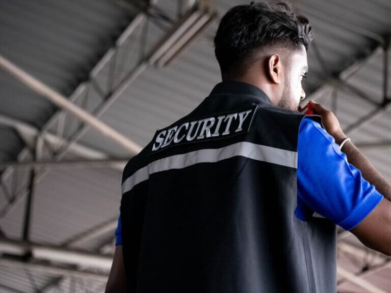 Manned Security person wearing black security gilet on radio to collegue from inside factory unit in Swansea South Wales
