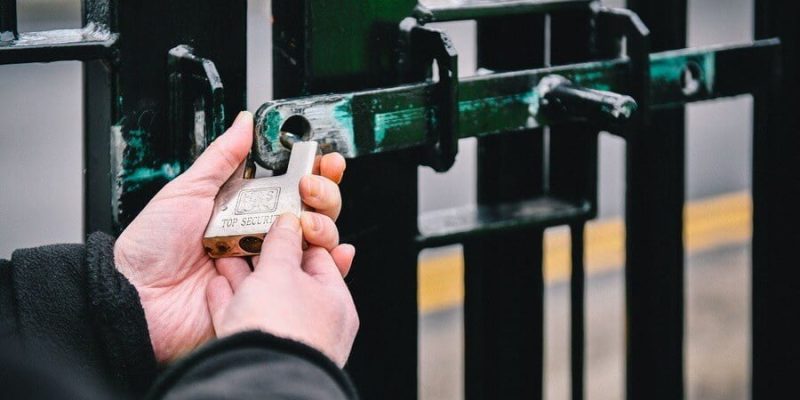 Security guard locking the gates of industrial unit with padlock