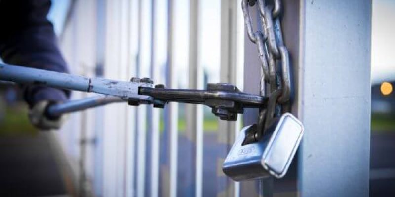 A burgular using a steel cutter to break a locked gate and enter a factory unit