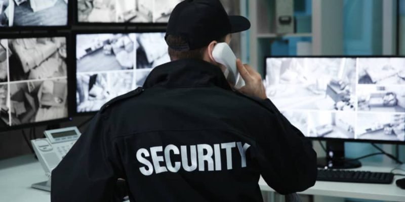 Security Guard on the telephone in front of 5 CCTV Security Monitors
