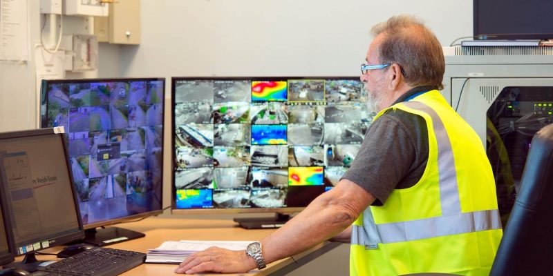 Security officer sitting at his desk wearing a high vis vest monitoring CCTV at a manufacturing site